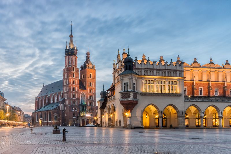 Wieczorny widok na Bazylikę Mariacką i Sukiennice na Rynku Głównym w Krakowie, z podświetlonymi detalami architektonicznymi.