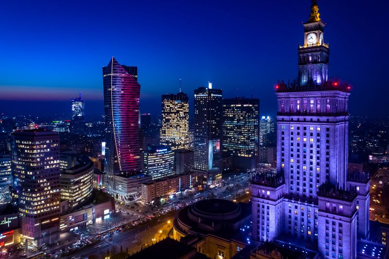 Night view of Warsaw's panorama with the illuminated Palace of Culture and Science and modern skyscrapers in the background.