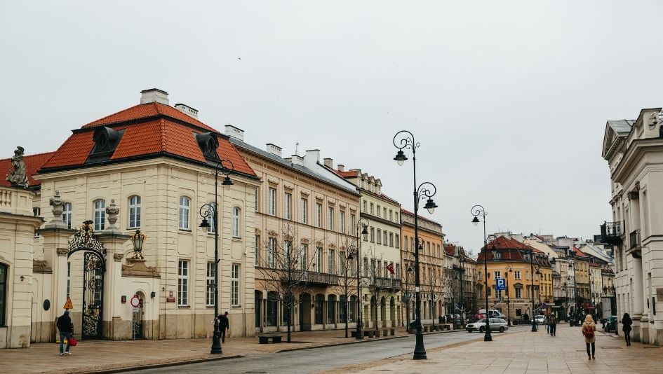 Ulica z zabytkowymi budynkami, ozdobnymi latarniami, brakiem liści na drzewach i kilkoma przechodniami na chodniku.