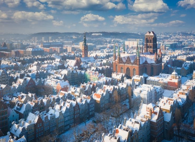 Widok na zaśnieżoną panoramę miasta z wyróżniającą się dużą, gotycką katedrą oraz wieżami kościołów na tle zachmurzonego nieba.
