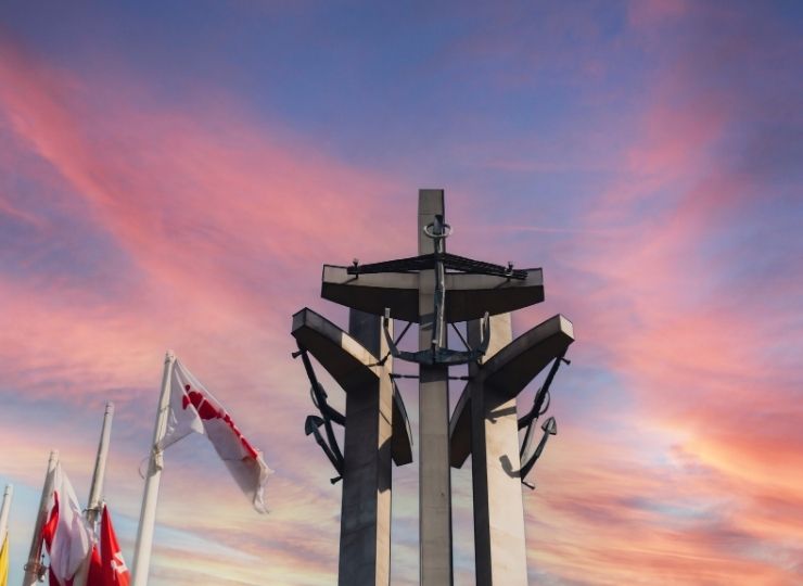A monument of three crosses against a colorful sunset, with flags waving in the wind on the left side.