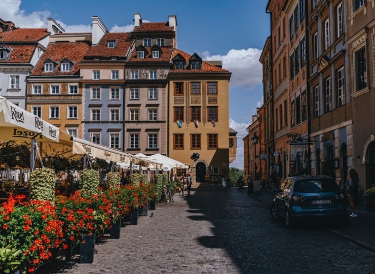 The Old Town in Warsaw with colorful townhouses, flowers and restaurant umbrellas on a cobblestone street, in sunny weather.