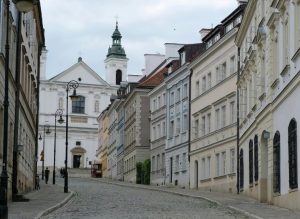A historic street of Warsaw in Poland with cobblestone pavement, leading to a white church with towers; on both sides there are colorful townhouses.
