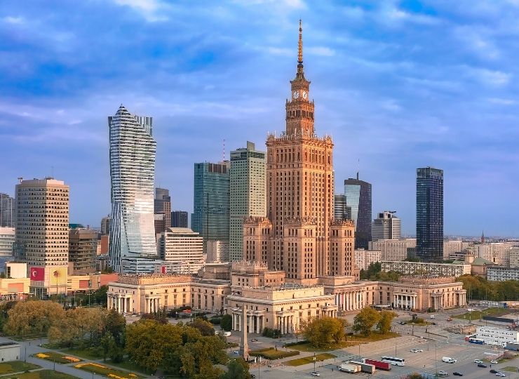 Warszawski Pałac Kultury i Nauki otoczony nowoczesnymi wieżowcami na tle nieba o zachodzie słońca.