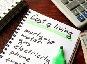 Notes listing 'Cost of living' along with items like mortgage, water, gas, electricity, and phone, highlighting expenses; a calculator and a green highlighter are nearby.