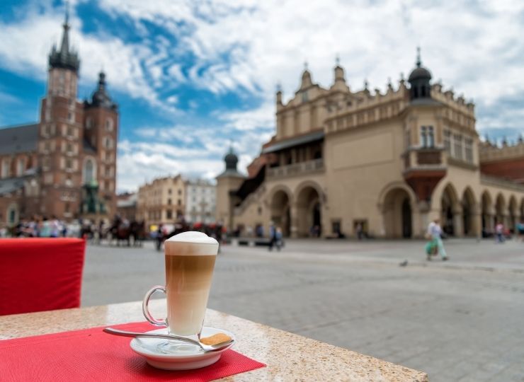 A cup of latte on a table in a café with a view of the Cloth Hall and St. Mary's Basilica in the Main Square in Krakow.