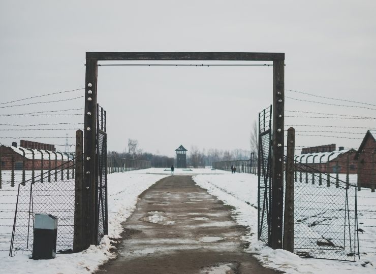 Winter view of the gate and barbed wire at Auschwitz concentration camp with a guard tower in the distance.