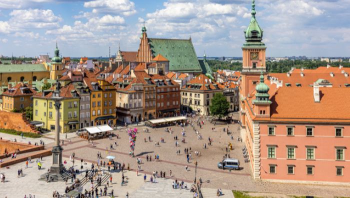 Aerial view of a busy square in Warsaw’s Old Town, Poland, featuring colorful historic buildings, red rooftops, and crowds of people—an ideal spot for sightseeing after using convenient luggage storage Warsaw offers.