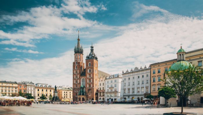 A wide view of Kraków’s Main Market Square, featuring St. Mary’s Basilica, historic buildings, a green-domed chapel, and crowds enjoying the day—perfect for sightseeing with luggage storage Krakow nearby for convenience.