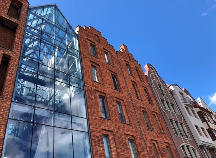 Nowoczesny ceglany budynek z dużą szklaną klatką schodową po lewej stronie, na tle błękitnego nieba z kilkoma obłokami. Architektura łączy styl tradycyjny ze współczesnym.